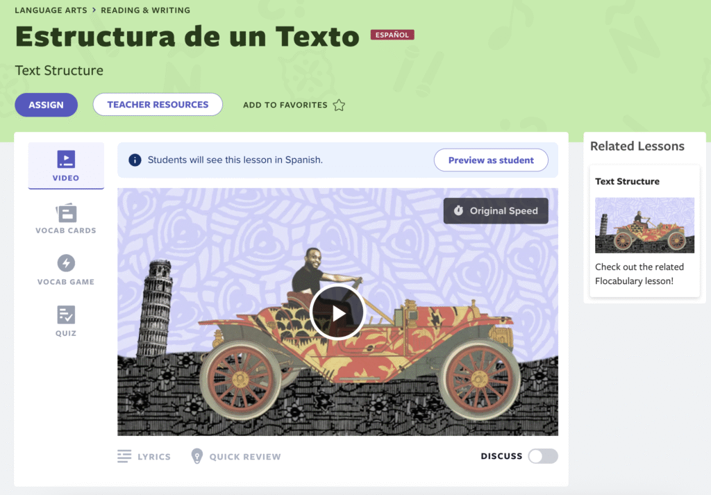 A screenshot of Flocabulary's Spanish version of the Text Structure lesson titled "Estructura de un Texto." The interface shows the same video content as the English version with an animated vintage car and the Leaning Tower of Pisa. A teacher view is displayed with a notification that "Students will see this lesson in Spanish" and a "Preview as student" button. Navigation includes Video, Vocab Cards, Vocab Game options, and related lessons appear on the right.